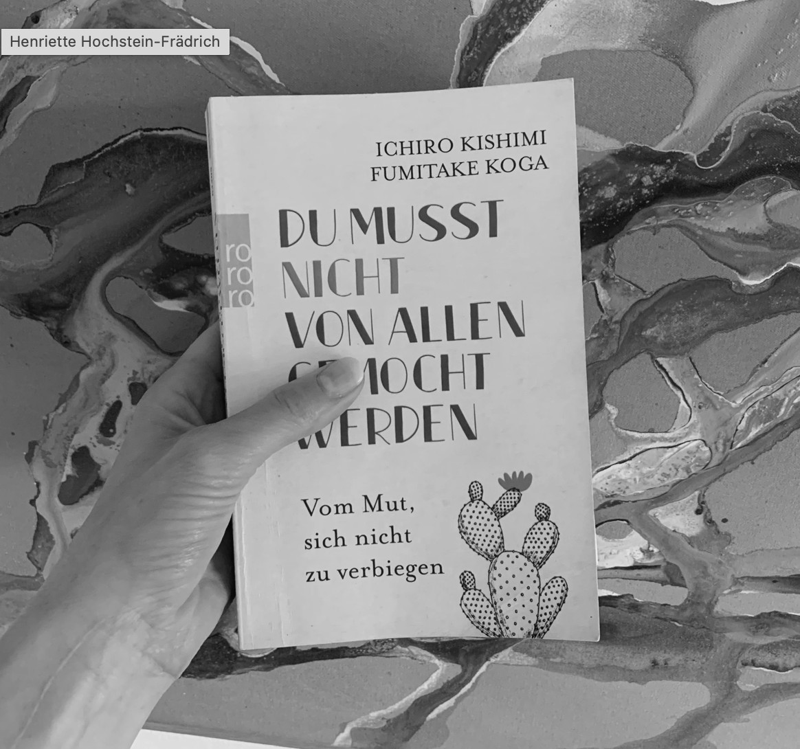 Cinematisches Schwarz-Weiß-Editorial-Stillleben auf dunklem Holz: ein aufgeschlagenes Buch mit einem warm-goldenen Schlüssel, der auf den Seiten liegt — der Schlüssel als einzige Farbe im monochromen Bild, Metapher für ein Buch als Schlüssel zu innerer Freiheit.